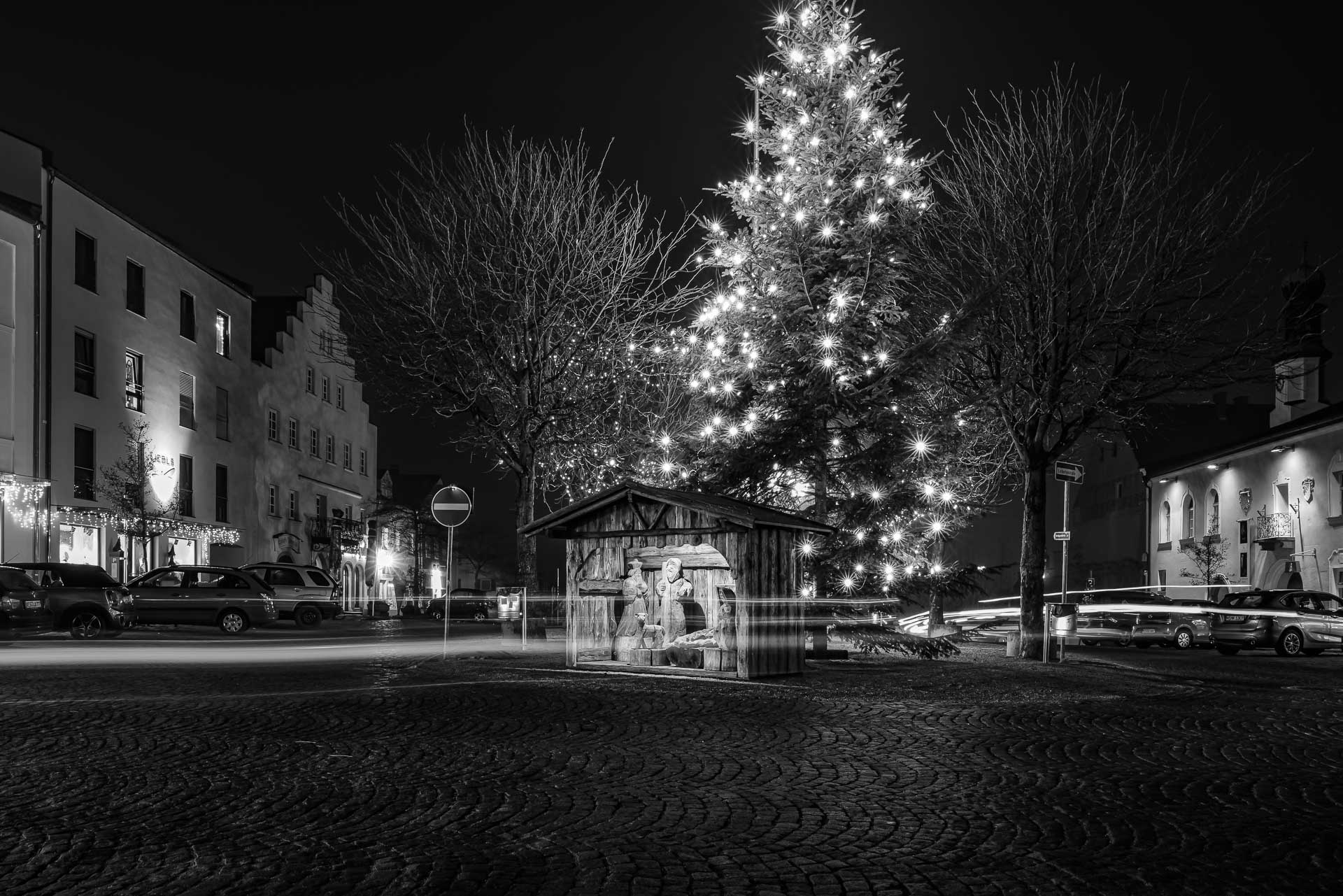 Nachts am Stadtplatz mit Weihnachtskrippe und beleuchtetem Weihnachtsbaum mit Lichtspuren von Autos